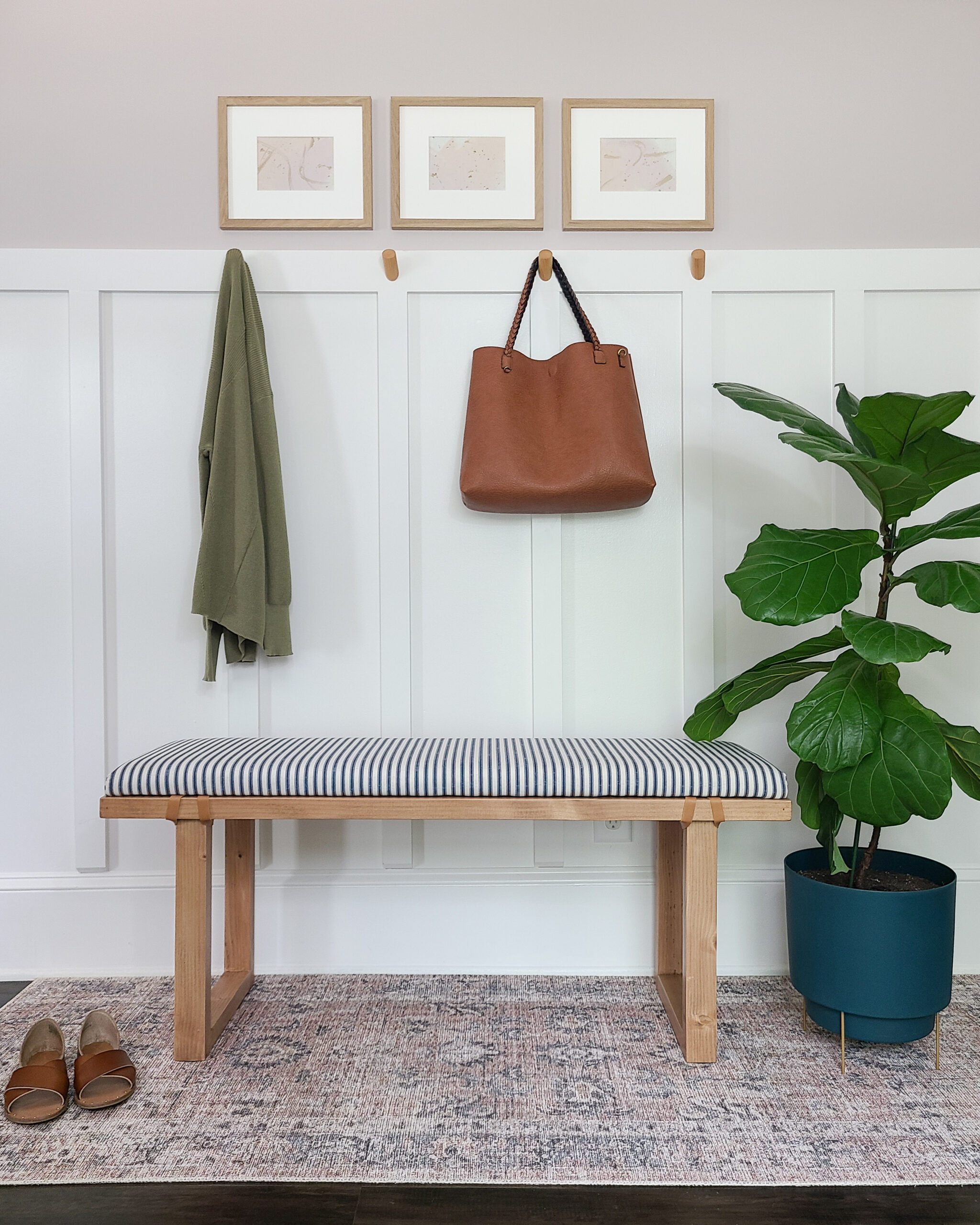 Entryway bench with a rug under it and a fiddle leaf fig tree next to it. 