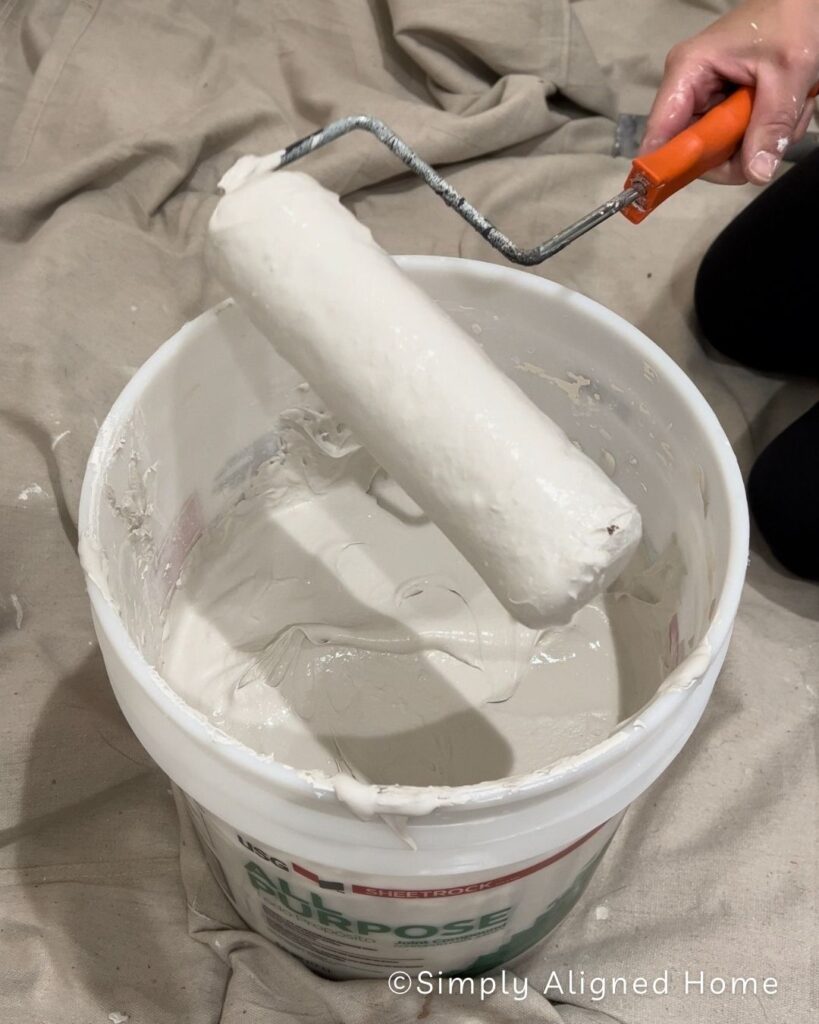 Using a paint roller to apply joint compound.